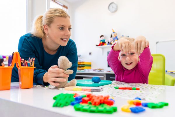 Toddler girl in child occupational therapy session doing sensory playful exercises with her therapist.